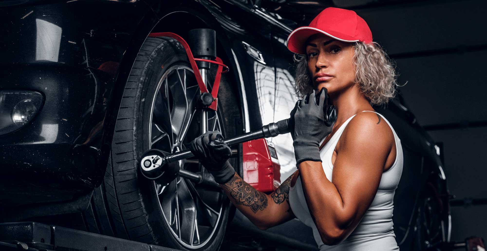 A woman in red hat holding a wrench near a tire.