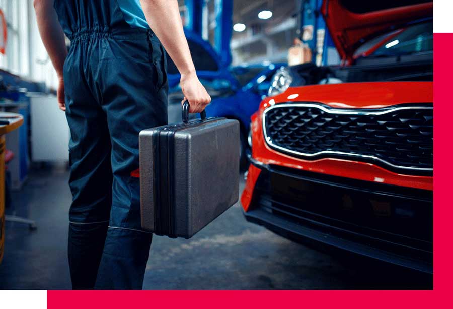 A person holding a tool box in front of a red car.